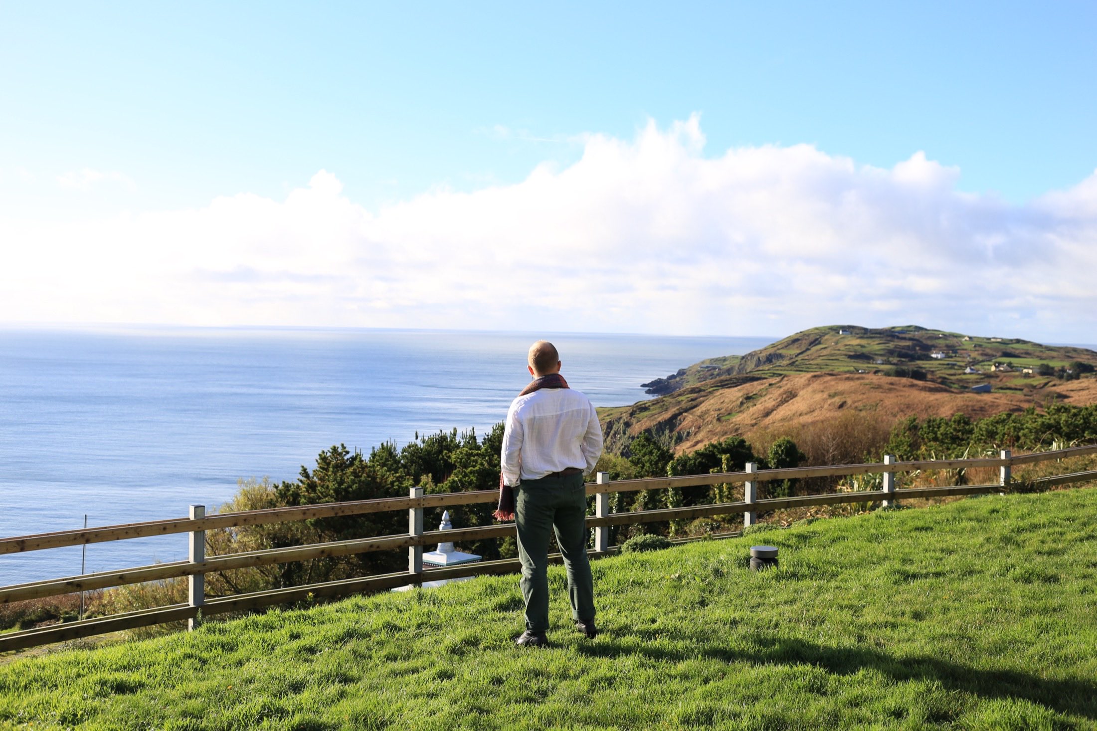Nico seen from behind at a coastal fence, looking out to sea toward a headland